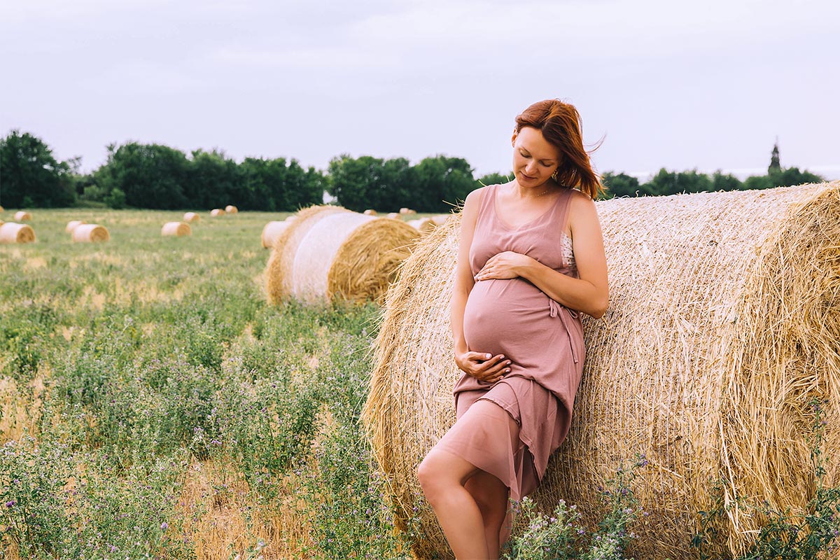 Schwangere Frau die sich in der Natur auf dem Weizenfeld mit Heuhaufen amüsiert an der Ostsee auf der Insel Rügen