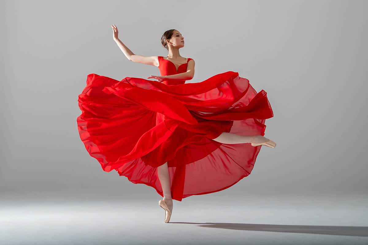 Fotograf Mazelle fotografiert eine junge, anmutige Ballerina, gekleidet in Spitzenschuhen und einem schwerelosen roten Rock, demonstriert ihre tänzerischen Fähigkeiten