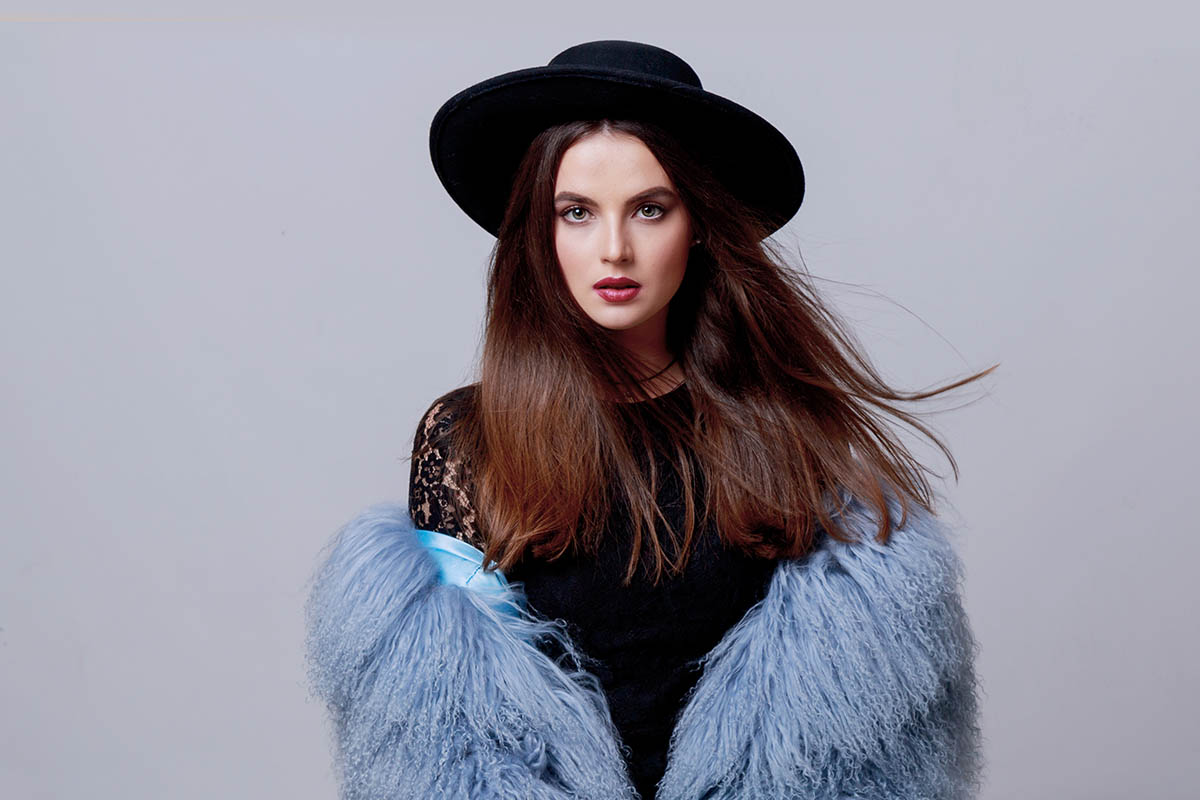 Modeporträt einer wunderschönen Fotomodel im stilvollen flauschigen blauen Wintermantel und schwarzem Hut fotografiert von Fotograf Mazelle